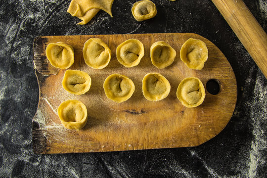 Freshly prepared Italian tortellini on wooden board top view
