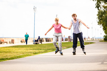 Obraz premium Young couple rollerblading in park holding hands.