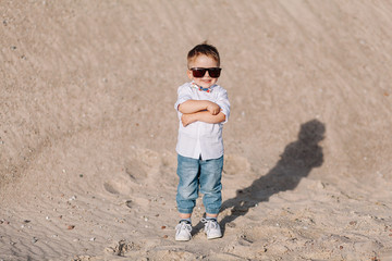 stylish little boy walks on the sand with sunglasses