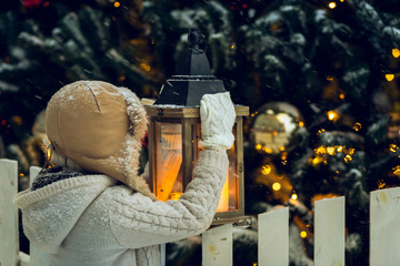 Child holding a lantern near Christmas tree at snowfall