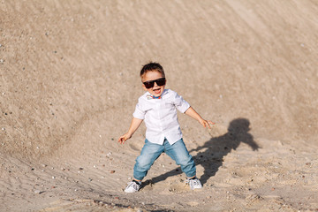 stylish little boy walks on the sand with sunglasses