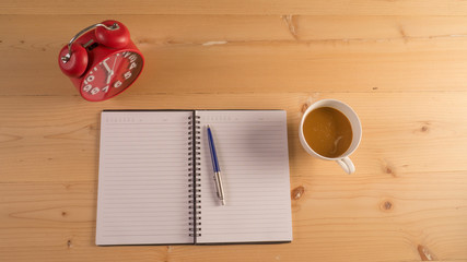 red alarm clock  books with notebook, pen and cup of coffee on