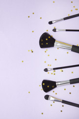 Various cosmetic make up brushes arrange on a pastel purple background with gold stars with empty space at side