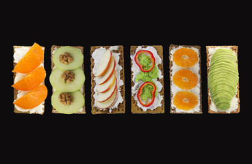 Sandwiches with cream cheese and fresh fruits and vegetables. Fresh healthy appetizer snack with crispbread on black background.
