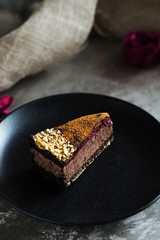 Piece of dark chocolate mousse cake with rose petal and blackberry jam on a black plate and stone background. Vegan, sugar, gluten free, dairy dessert. Vertical