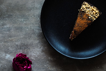 Piece of dark chocolate cake with rose petals on a black plate and stone background. Dark food...