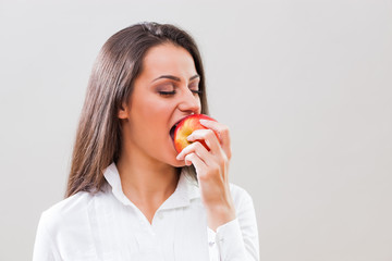 Studio shot portrait of young businesswoman who is eating an apple. 