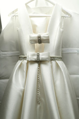 Whtie wedding dress decorated with bows and crystals hangs on pe