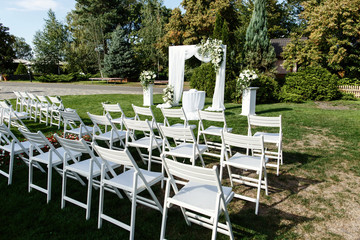 White garden chairs stand in rows before wedding altar decorated