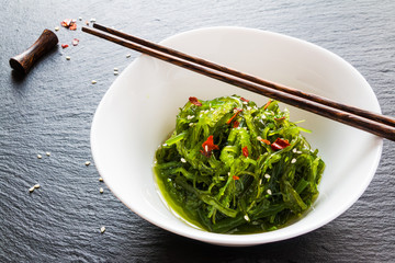 Chuka wakame, seasoned sesame seaweed japanese salad in white bowl and chopsticks on black stone. © Magrig