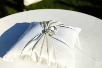 Silver wedding rings lie on white pillow decorated with crystals