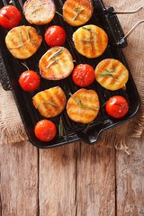 Tasty roasted potatoes and tomatoes with rosemary close up on a grill pan. Vertical top view