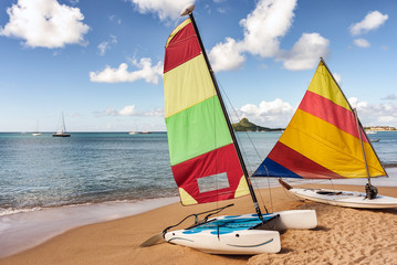Colorful sail boat and catamaran rest on sandy beach