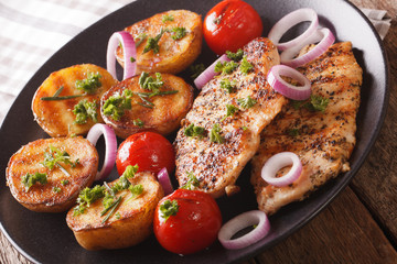 Delicious food: fried chicken breast with grilled potatoes and tomatoes close-up on a plate. horizontal