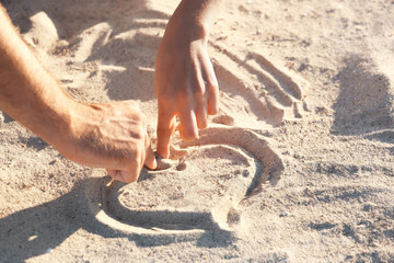 Two hands drawing heart on sand, closeup