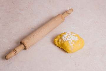 Rolling pin and yellow dough with white flour on light marble ba