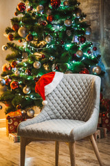 Fototapeta na wymiar Beautiful New year room with a Christmas tree and a chair with a Santa hat