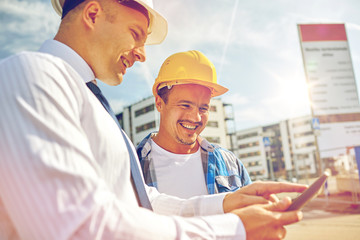 happy builders in hardhats with tablet pc outdoors