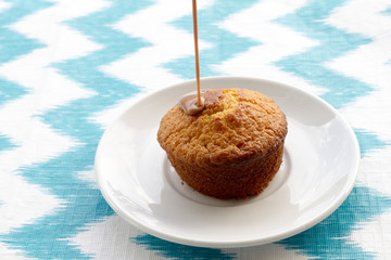 Chocolate is poured onto cake at plate on striped background. To