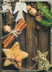 Sweet holiday gingerbread star shaped cookies, wooden angels, decorative golden stars, nuts, tied cinnamon sticks and fir-tree branch on rustic wooden tray background, top view, copy space