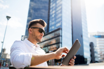 man with tablet pc sitting on city street bench