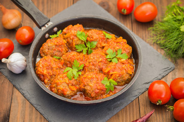 Meatballs in sweet and sour tomato sauce in the pan. Wooden background. Close-up