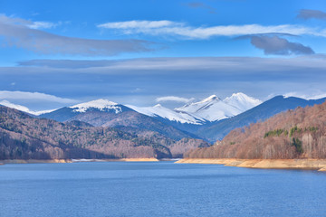Mountain lake panorama against cloudy sky and mountains covered
