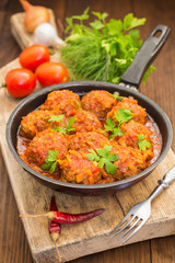 Meatballs in sweet and sour tomato sauce in the pan. Wooden background. Close-up