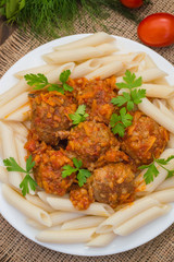 Meatballs with pasta penne in tomato sauce on a white plate. Wooden rustic background. Top view. Close-up