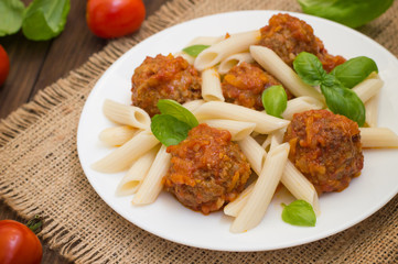 Meatballs with pasta penne in tomato sauce on a white plate. Wooden rustic background. Top view. Close-up