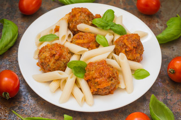 Meatballs with pasta penne in tomato sauce on a white plate. Wooden rustic background. Top view. Close-up