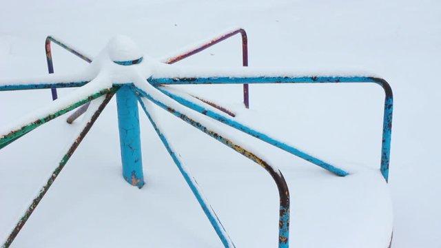 Deserted old children playground with peeling paint in winter city park covered with snow. No people. Real time full hd video footage.