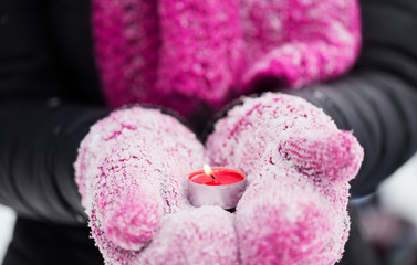 close up of hands in winter mittens holding candle