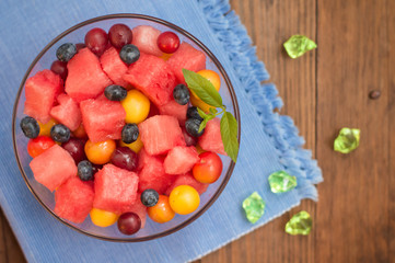 Fototapeta na wymiar Fruit and berry salad of watermelon, blueberries, plums, currants, gooseberry, cherry plum. Wooden background. Top view. Close-up