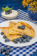 Pancakes with blueberries, whipped cream and a sprig of mint  lemon balm. Wooden blue background. Close-up.