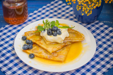 Pancakes with blueberries, whipped cream and a sprig of mint  lemon balm. Wooden blue background. Close-up.