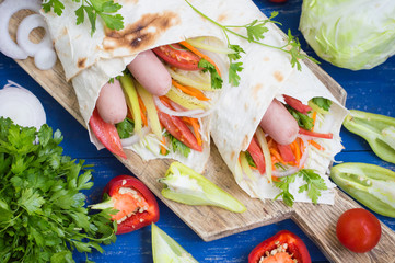 Hot dog - sandwich with sausage in pita, Korean carrots, tomatoes, onions, parsley and pepper. Wooden background. Closeup