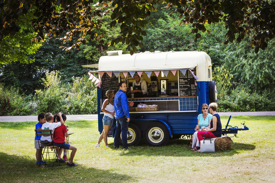 People around a blue mobile coffee shop on a lawn.