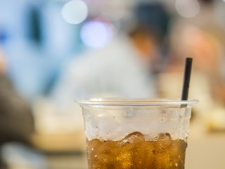 Closeup of plastic glass of cola with blurry food court
