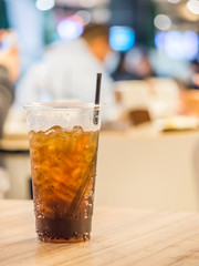 Plastic glass of cola on wooden table with blurry food court