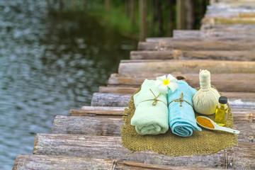 Spa herbal compressing ball , white frangipani flowers, turmeric powder in white spoon massage oil and blue faric in sisal on bamboo background and river side.