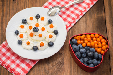 Blueberries and buckthorn laid out in the shape of a heart with cream meringue. Wooden background. Top view. Close-up