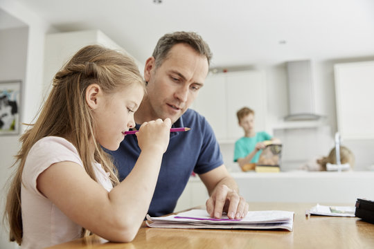A young girl and her father sitting looking at her school books, doing her homework. 