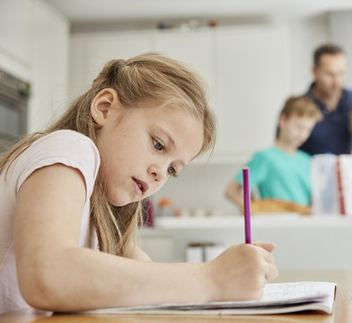 Girl sitting at table in family kitchen, doing her homework