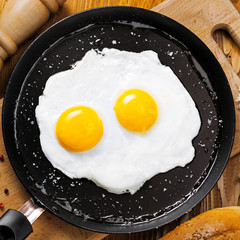 Two fried eggs in a frying pan cooked for breakfast. Delicious international meal on a table. Homemade food, top view.