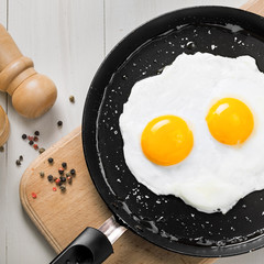 Two fried eggs in a frying pan cooked for breakfast. Delicious international meal on a table. Homemade food, top view.