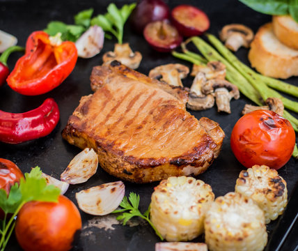 Steak on the bone with vegetables cooked  the grill. Black stone background. Top view. Selective focus close-up