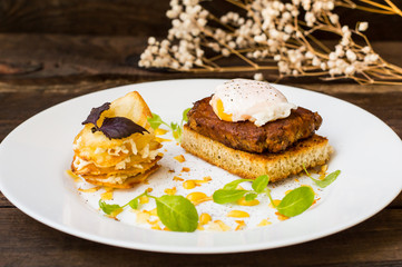 Dish with meat steak on toast, potato chips  melted cheese and poached egg  Dutch sauce. Wooden background. Top view. Close-up