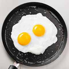 Traditional healthy easy quick breakfast meal made of two fried eggs served on a frying pan. International simple food, top view.