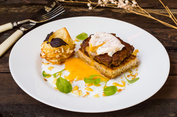 Dish with meat steak on toast, potato chips  melted cheese and poached egg  Dutch sauce. Wooden background. Top view. Close-up